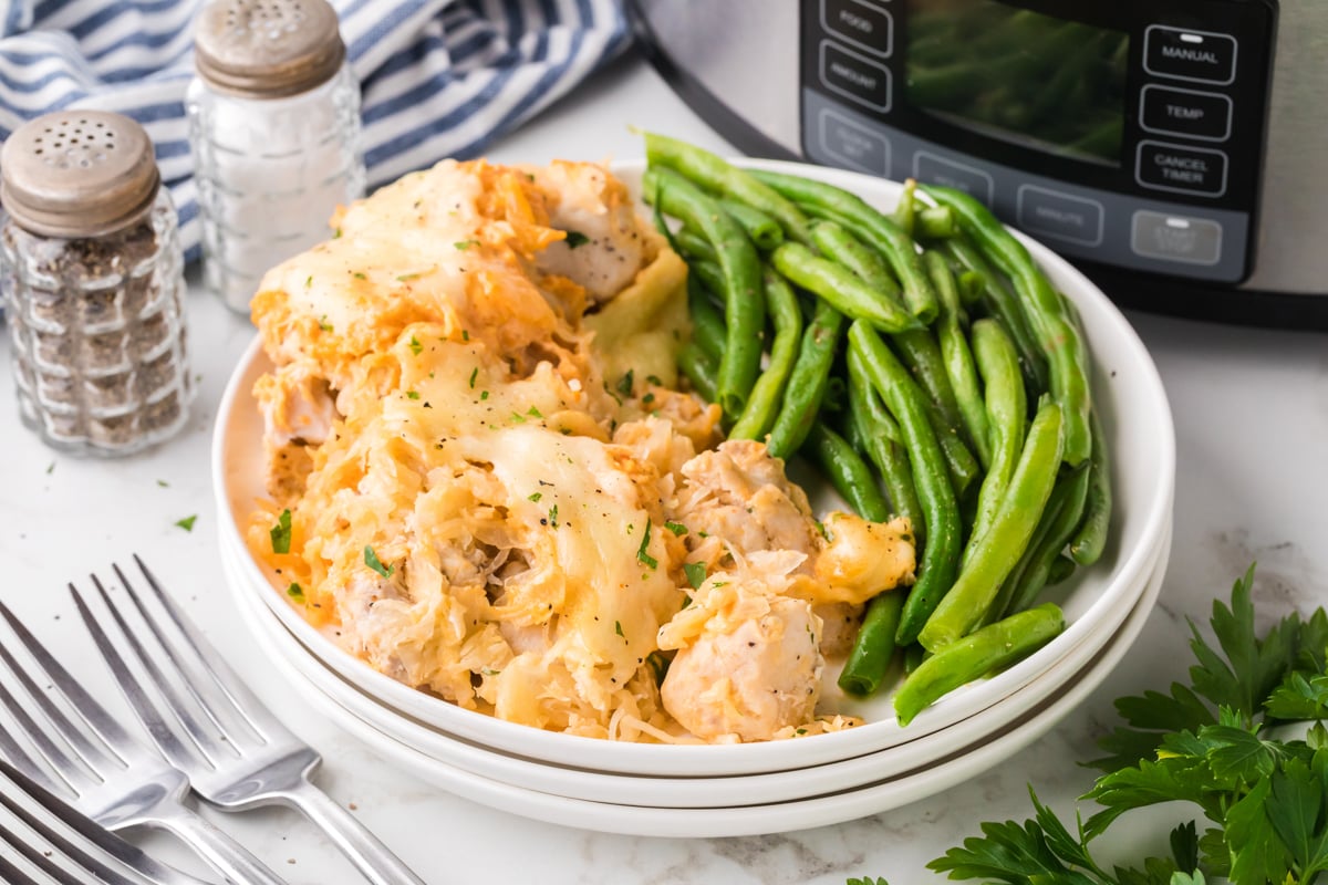 Serving of slow cooker chicken reuben casserole  with green beans on a stack of white plates.