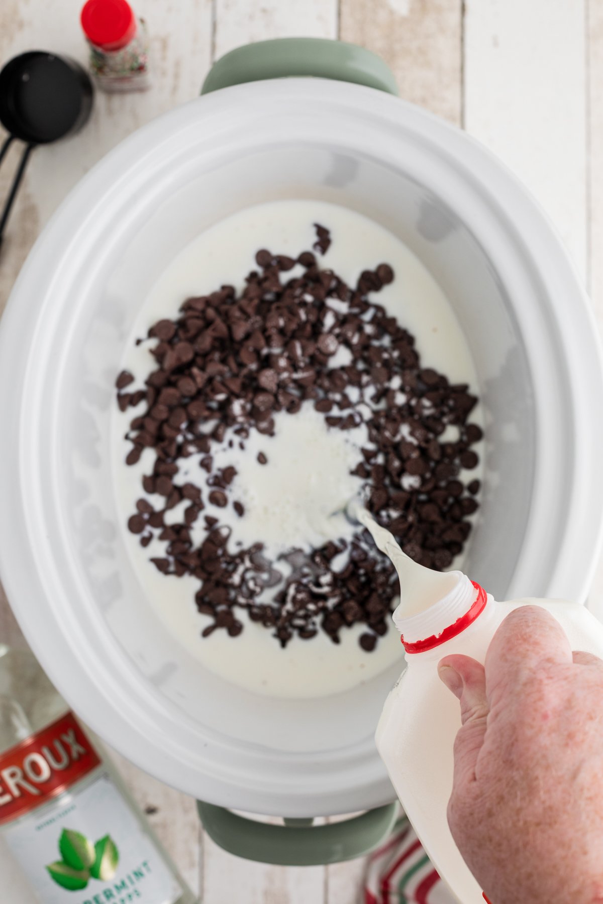 Pouring milk into a crockpot with chocolate chips and sugar.