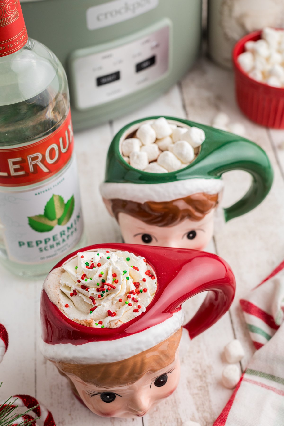 2 mugs of boozy hot chocolate in front of a slow cooker.