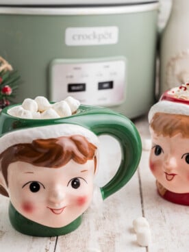 Slow cooker boozy hot chocolate in festive mugs in front of a crockpot.