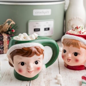 Slow cooker boozy hot chocolate in festive mugs in front of a crockpot.