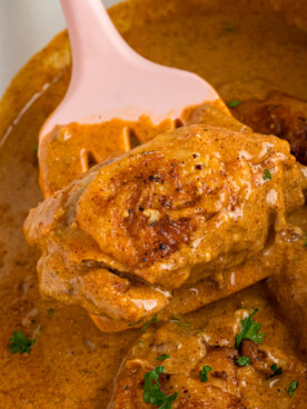 A piece of slow cooker chicken paprika being held up with a spatula.