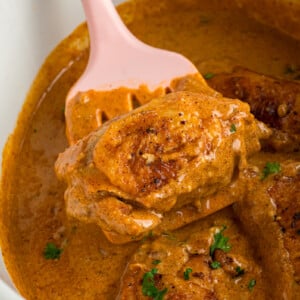 A piece of slow cooker chicken paprika being held up with a spatula.