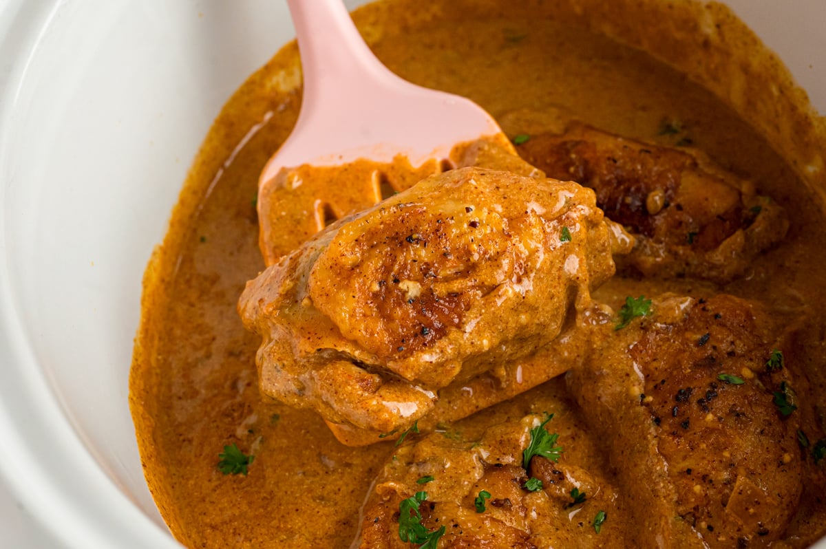A piece of slow cooker chicken paprika being held up with a spatula.