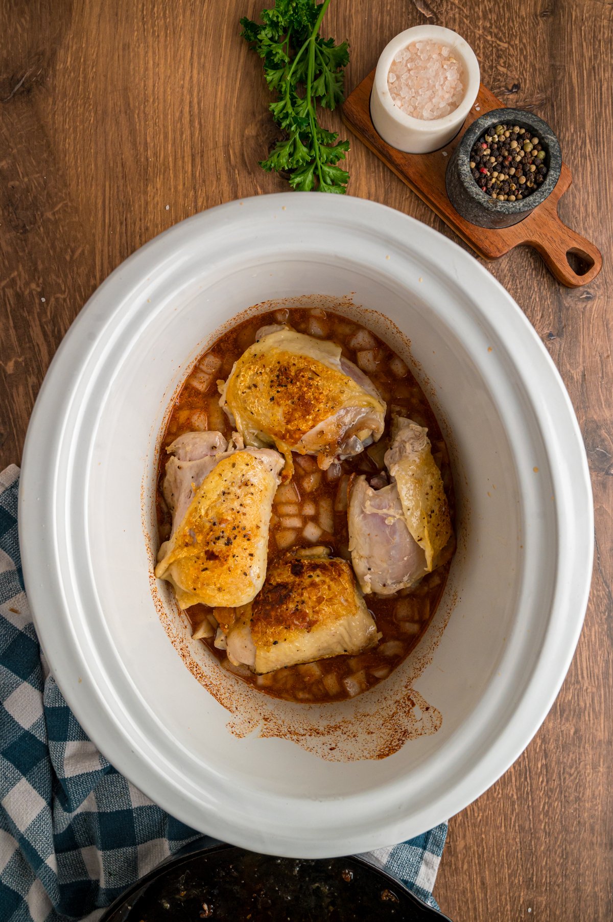 Seared chicken thighs on top of broth mixture in a crockpot.