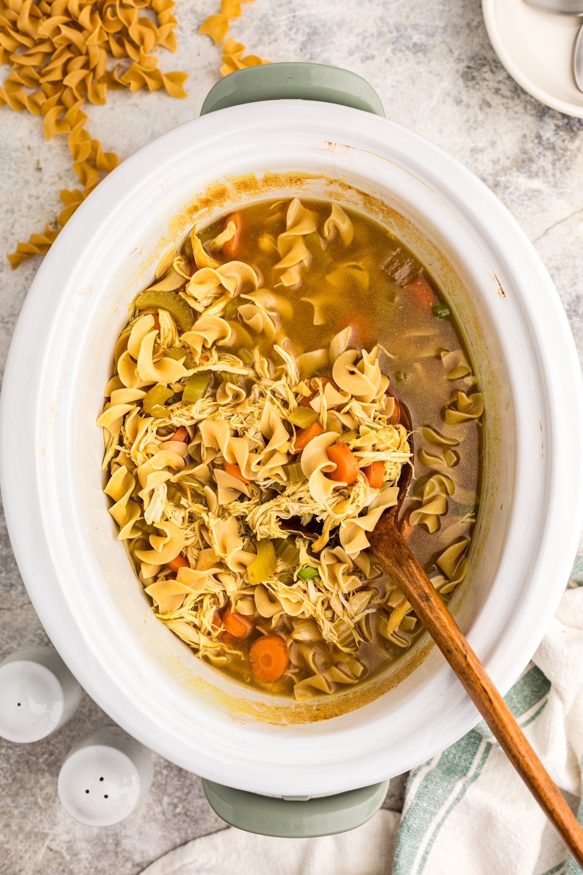 Slow cooker curried chicken noodle soup in a crockpot with a wooden spoon in it.