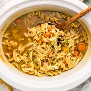 Wooden spoon scooping up some slow cooker curried chicken noodle soup.