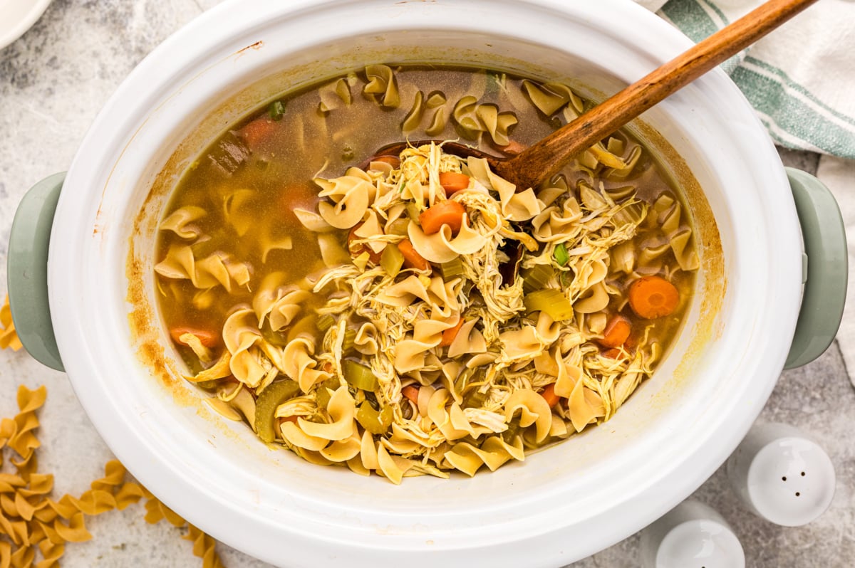 Wooden spoon scooping up some slow cooker curried chicken noodle soup.
