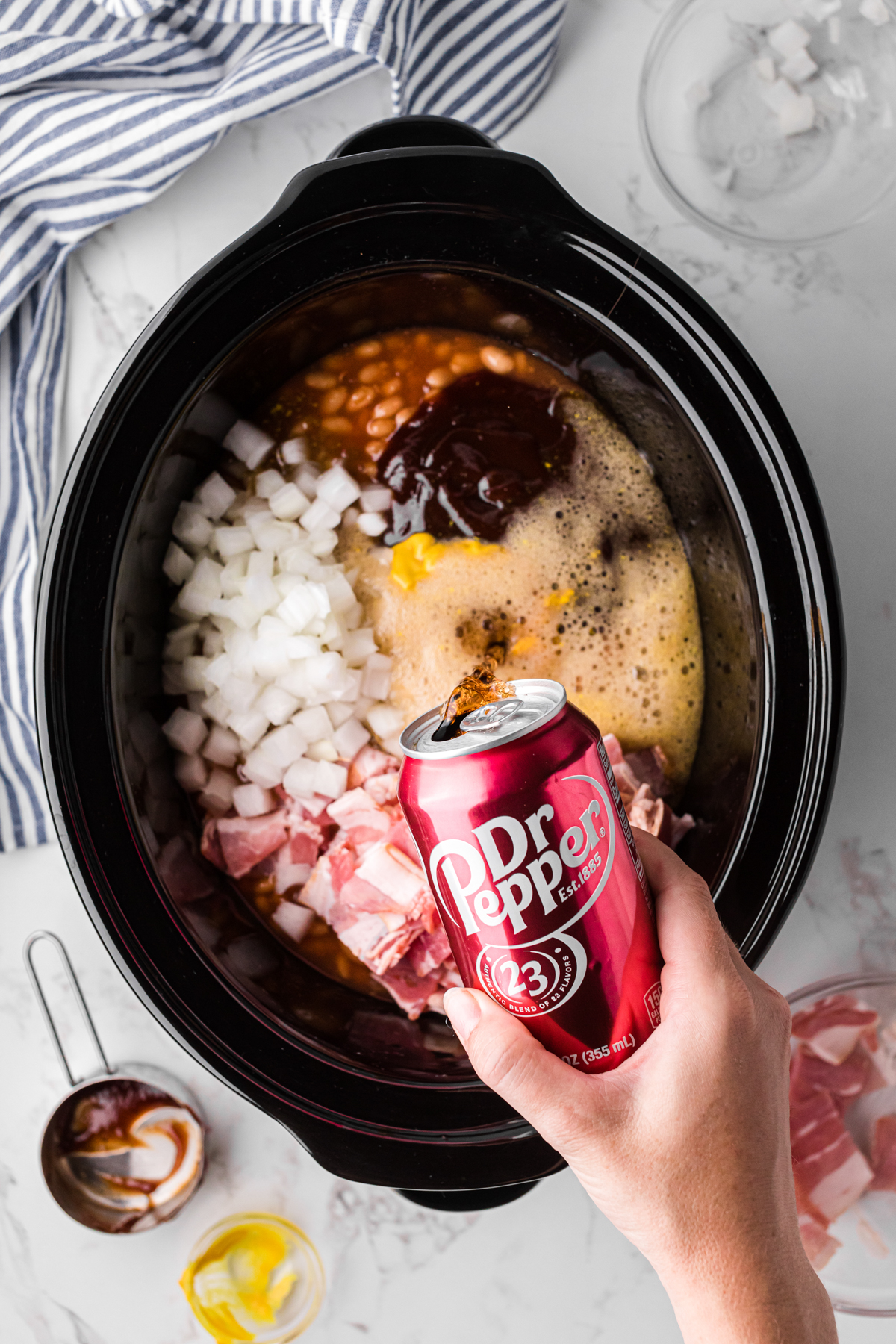 adding dr. pepper to the ingredients for slow cooker dr. pepper baked beans in a crockpot.