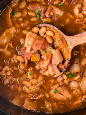 close-up of slow cooker dr. pepper baked beans with a wooden spoon.