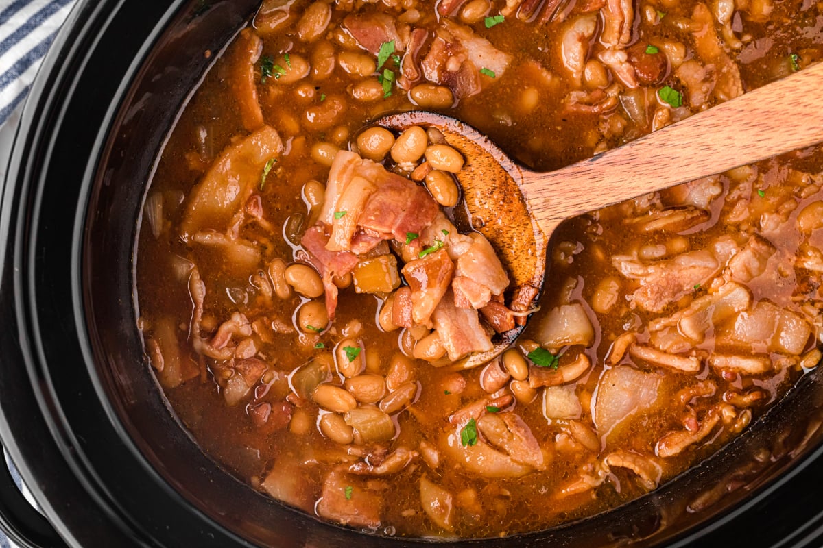 close-up of slow cooker dr. pepper baked beans  with a wooden spoon.