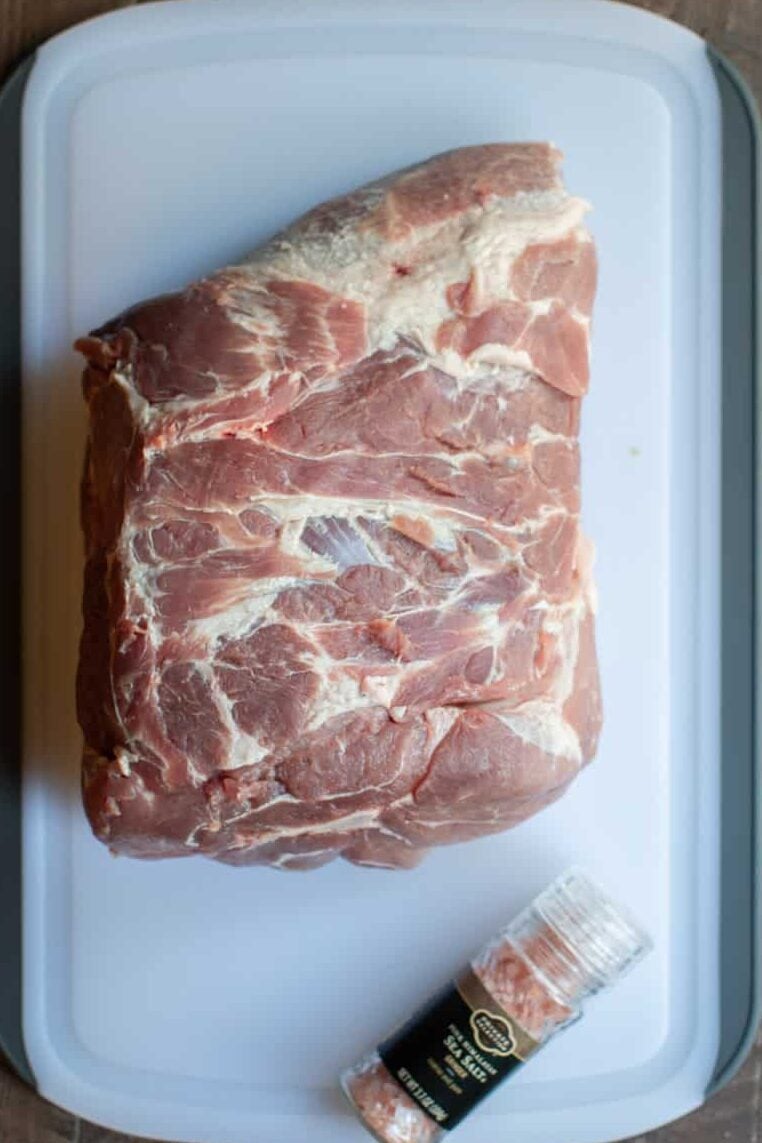Pork roast unwrapped on a cutting board with jar of Himalayan sea salt next to it.
