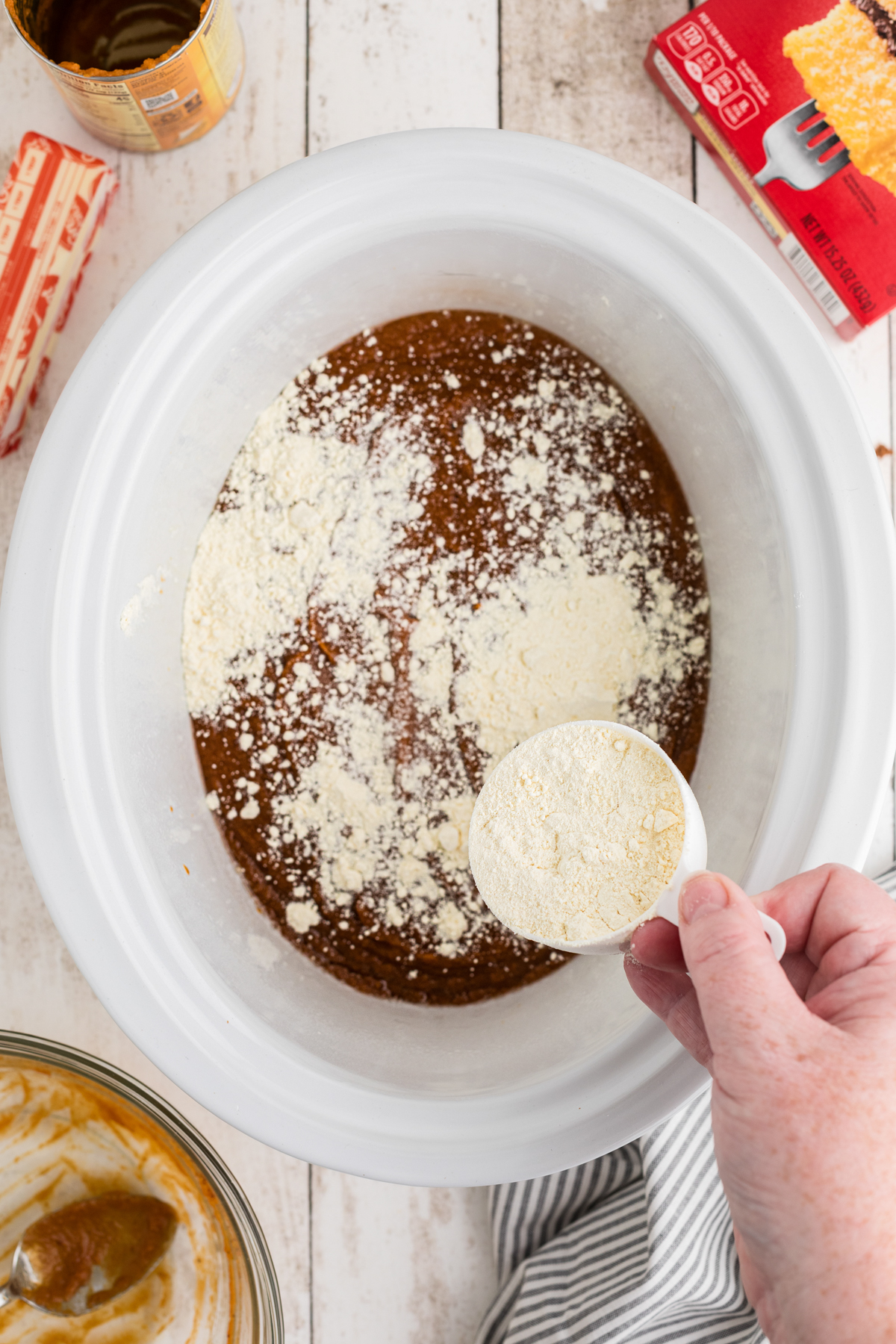 Cake mix being added to the pumpkin mixture in a crockpot.