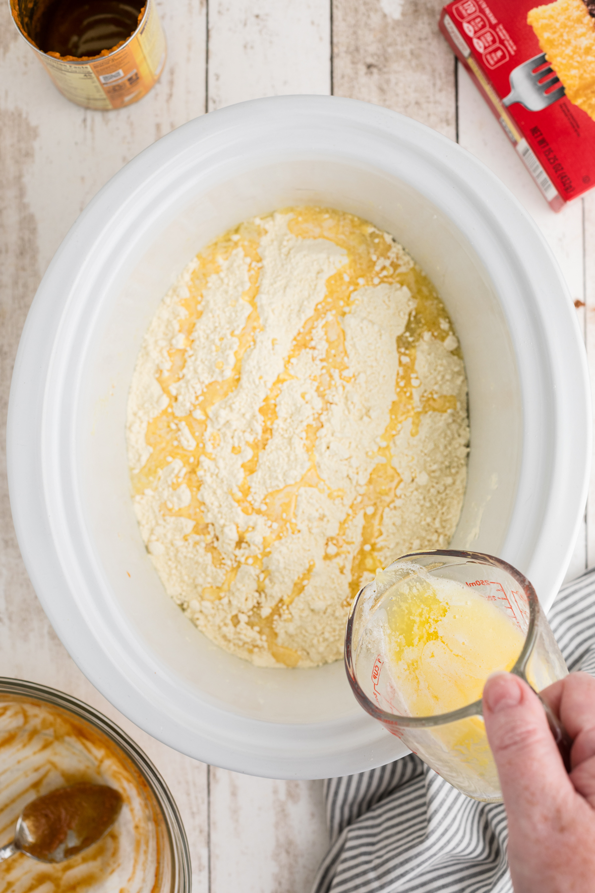 Melted butter being poured onto cake mix in a crockpot.