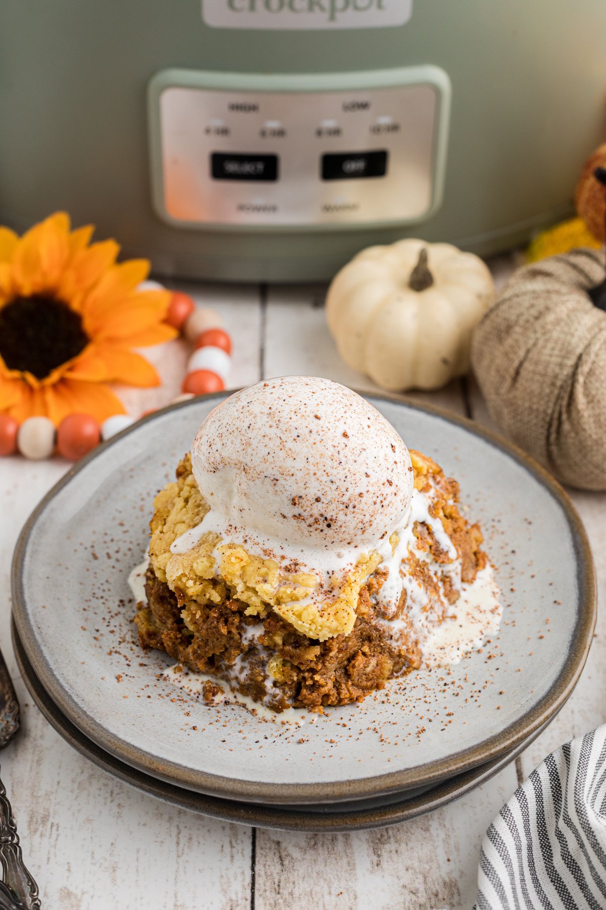 Slice of slow cooker pumpkin cobbler with ice cream on top on a plate.