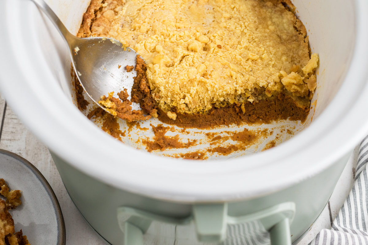 Slow cooker pumpkin cobbler in a crockpot with a spoon.