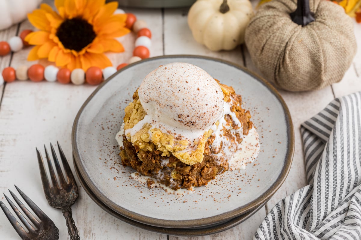 Slow cooker pumpkin cobbler on a plate with ice cream on top melting down the sides.