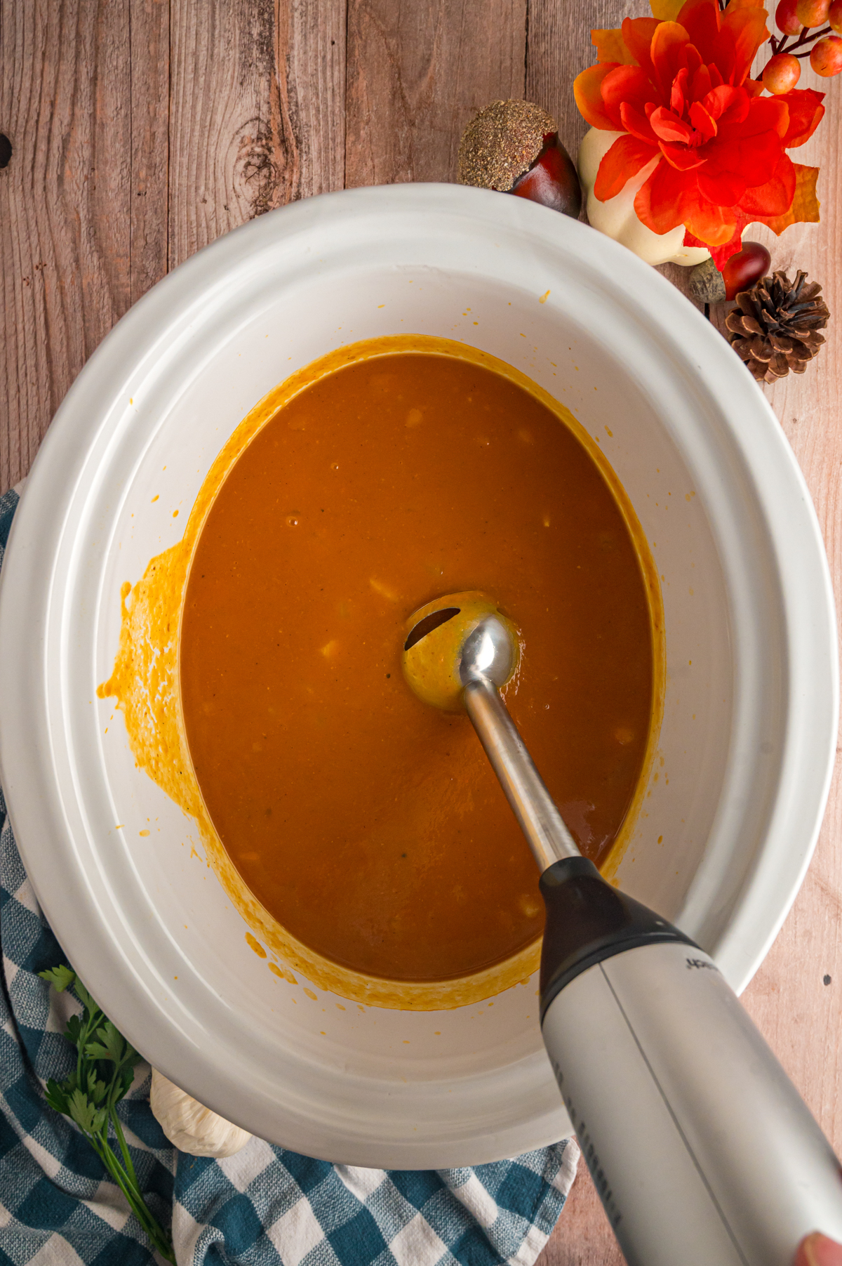 Using an immersion blender to puree pumpkin soup in a crockpot.