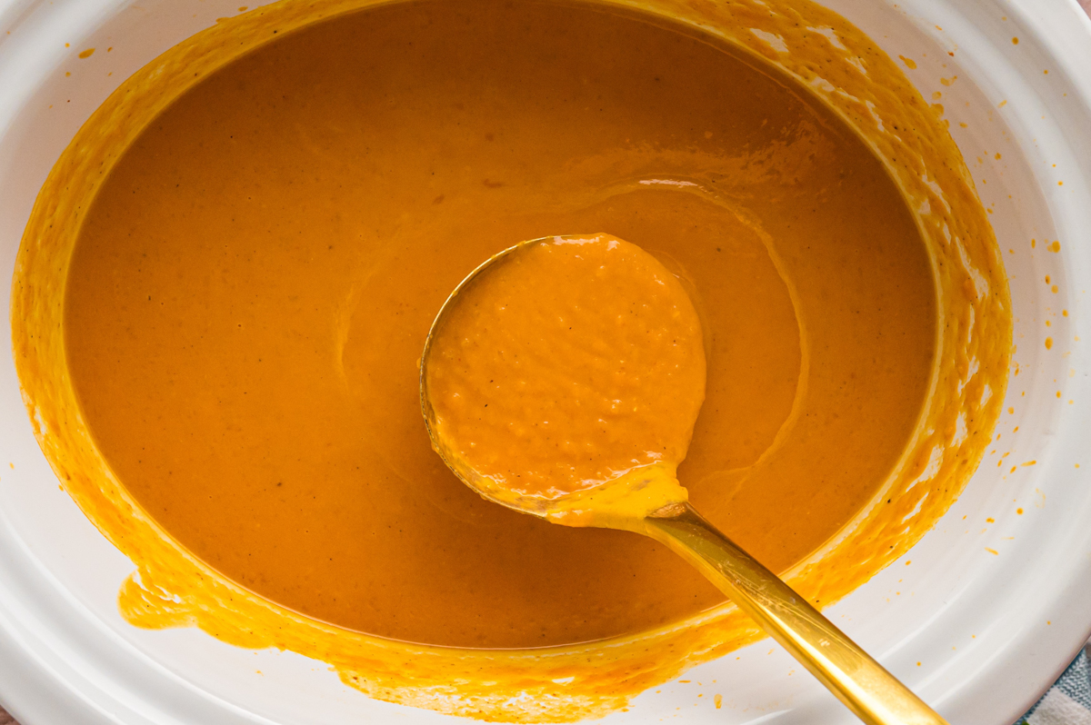 Ladle scooping out pumpkin soup from a slow cooker.