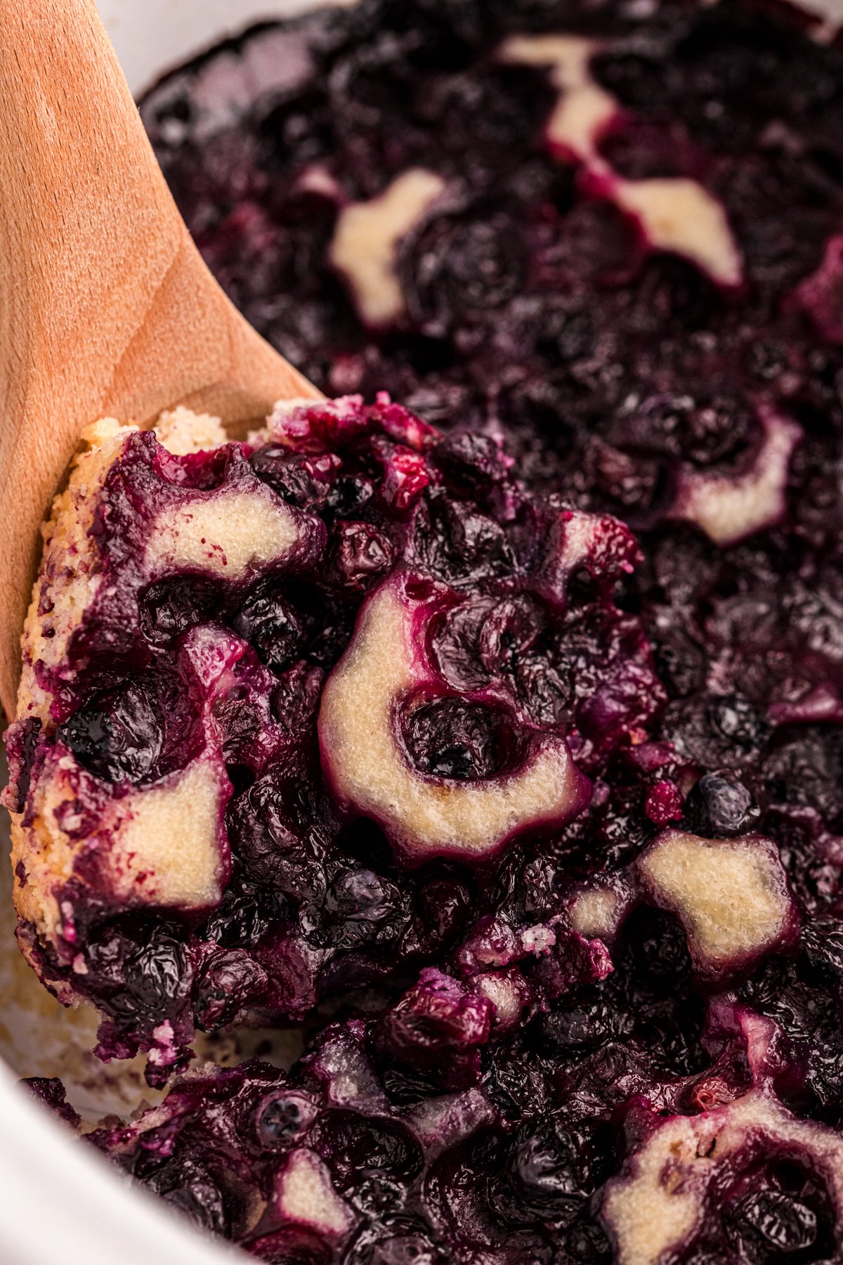 Close-up of a wooden spoon scooping out some slow cooker blueberry cobbler.