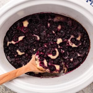 Slow cooker blueberry cobbler with a wooden spoon in it.