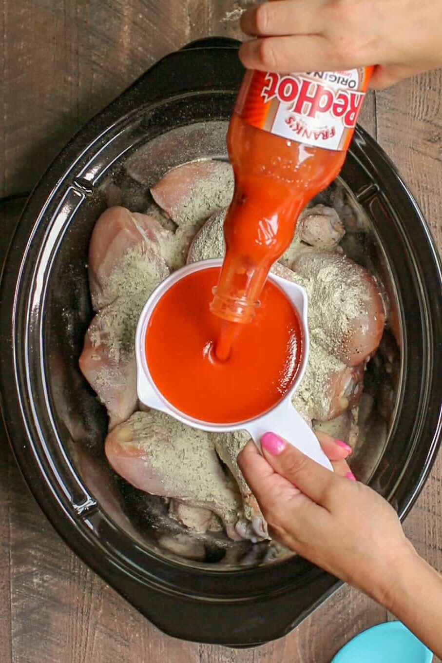 buffalo sauce being pour into a measuring cup over drumsticks in the slow cooker