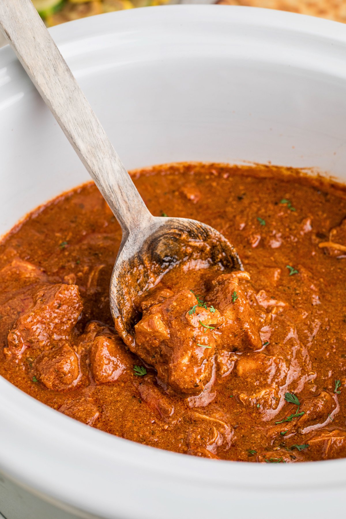 Slow cooker chicken curry in a crockpot with a wooden spoon.