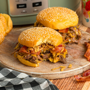Two slow cooker cowboy sandwiches on a serving plate with a bite taken out of one.