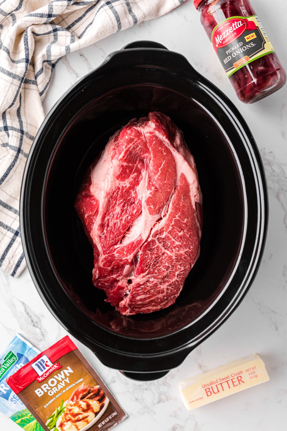 Raw chuck roast in a slow cooker.