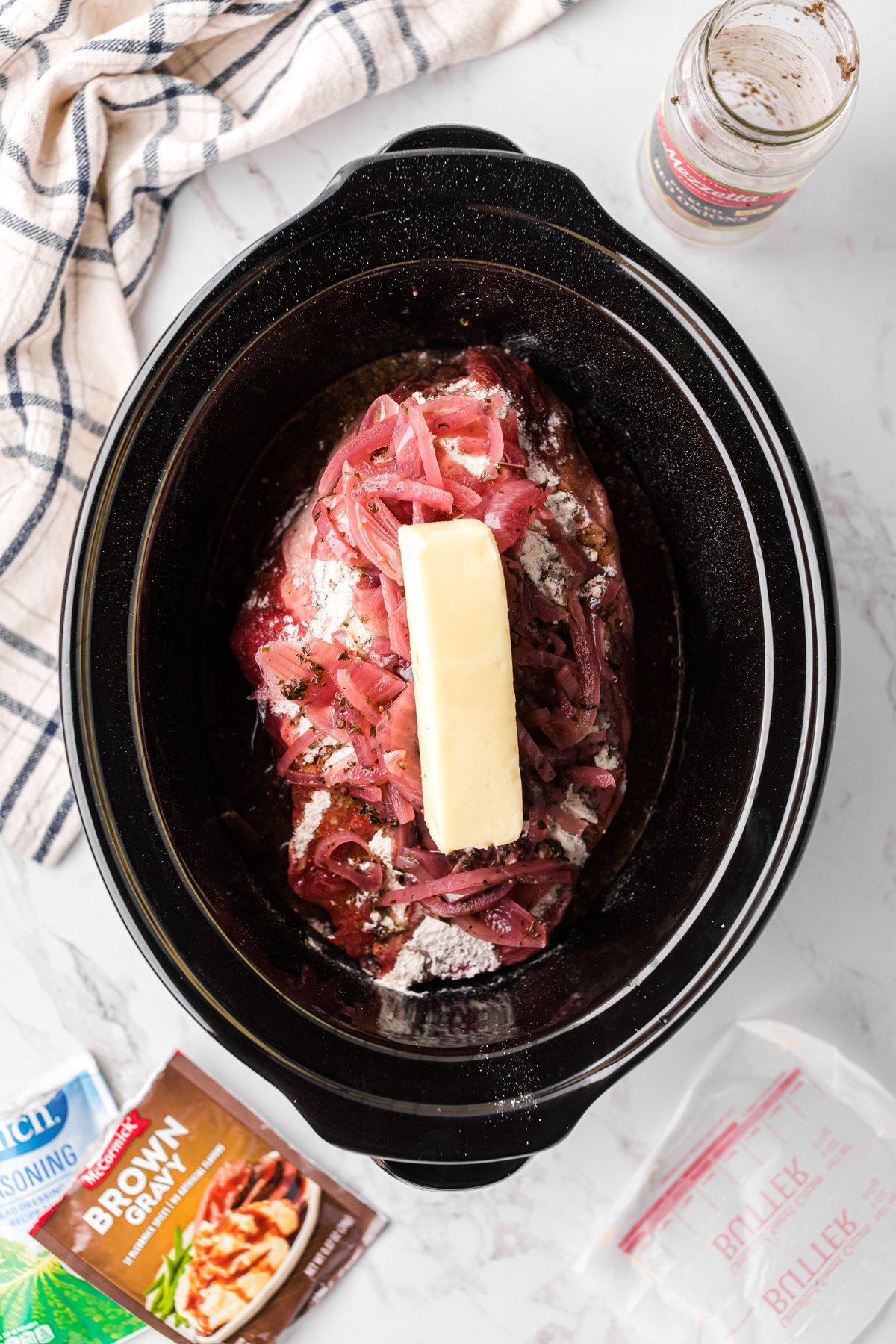 Pickled onions and butter added to a seasoned chuck roast in a crockpot.