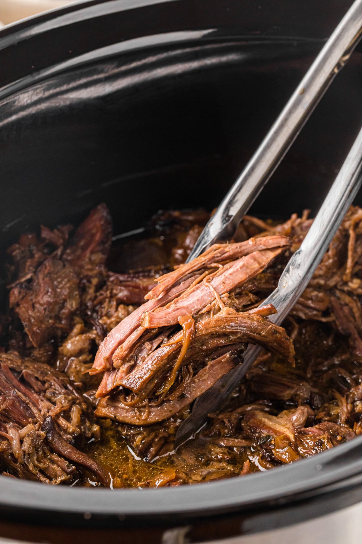 Tongs grabbing some slow cooker georgia pot roast.