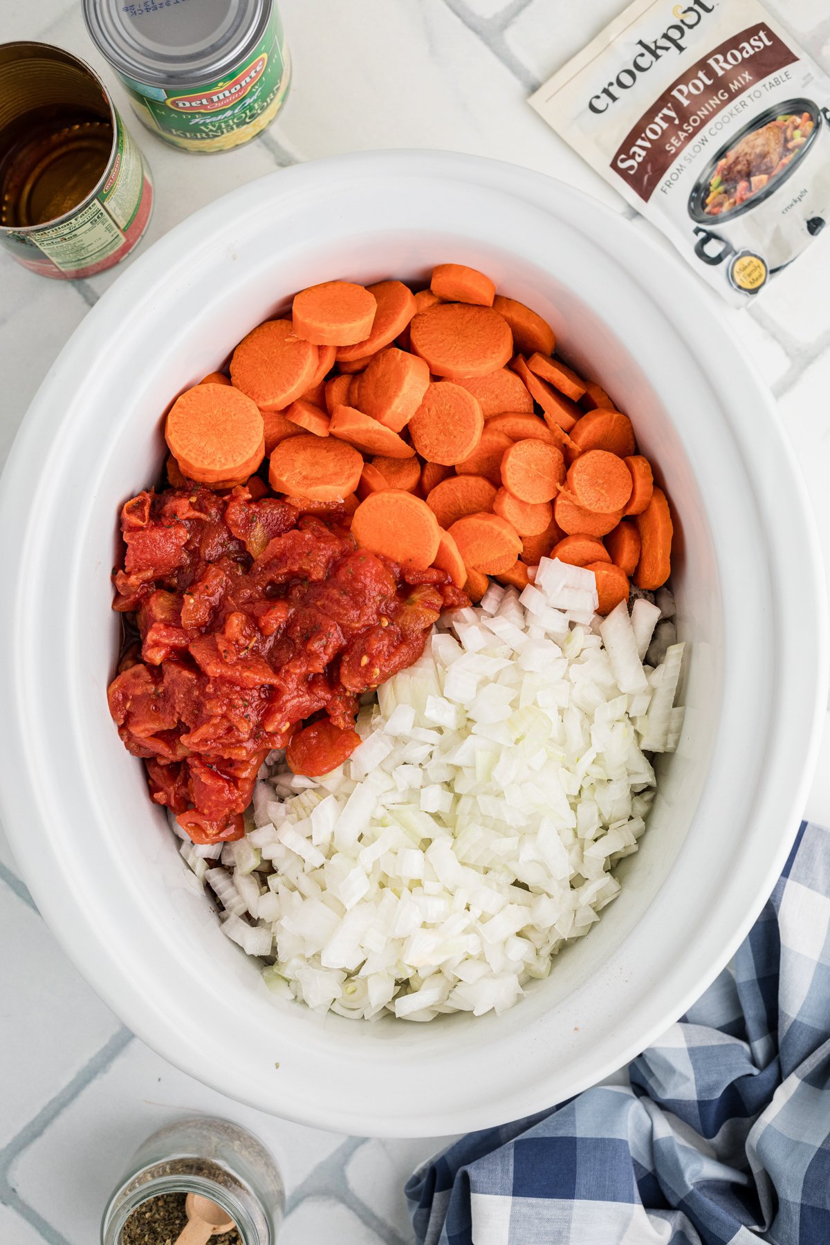 Carrots, diced tomatoes, and onion added to seasoned meat in a crockpot.