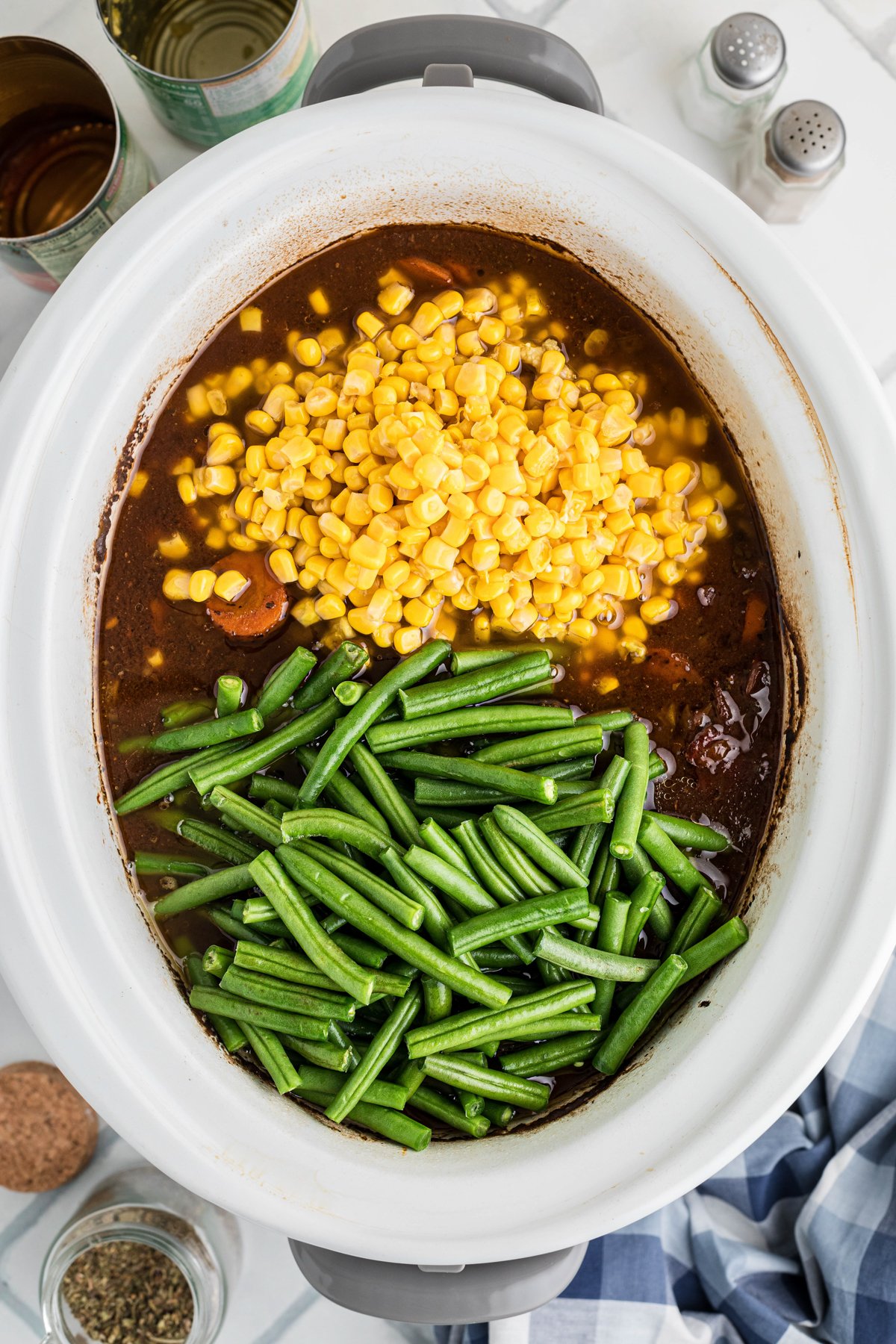Green beans and corn added to meat and veggie mixture in a crockpot.