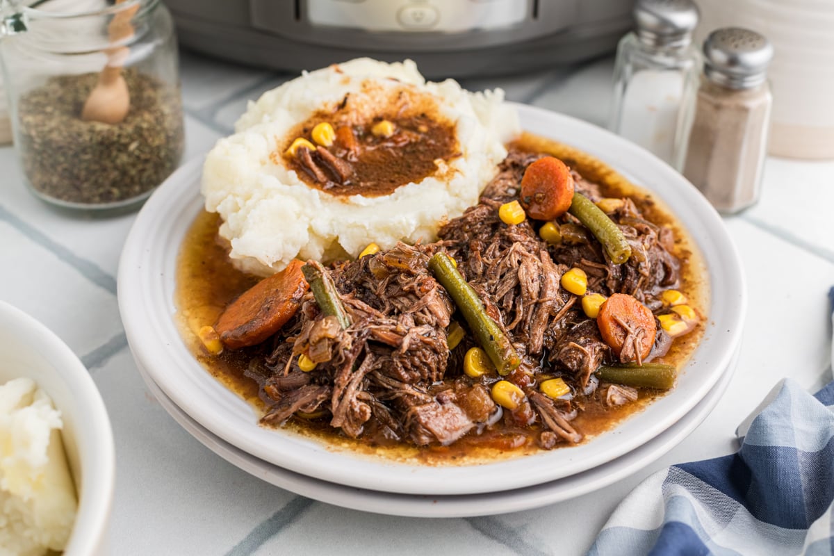 Slow cooker shredded beef dinner on a white plate with mashed potatoes.