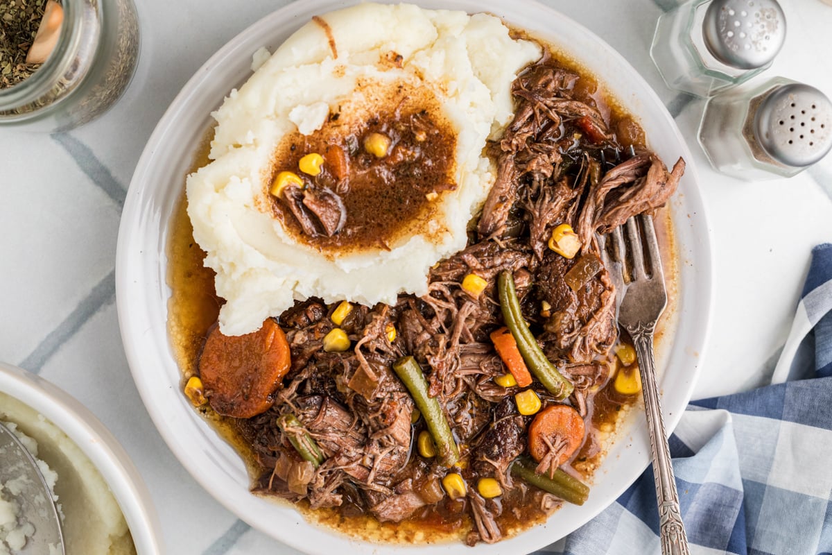 A serving of slow cooker shredded beef dinner on a plate with mashed potatoes.