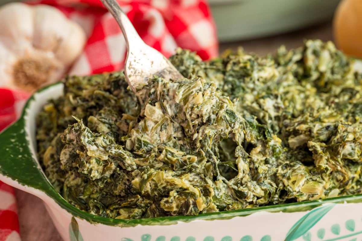 A fork grabbing some slow cooker creamed spinach from a casserole dish.