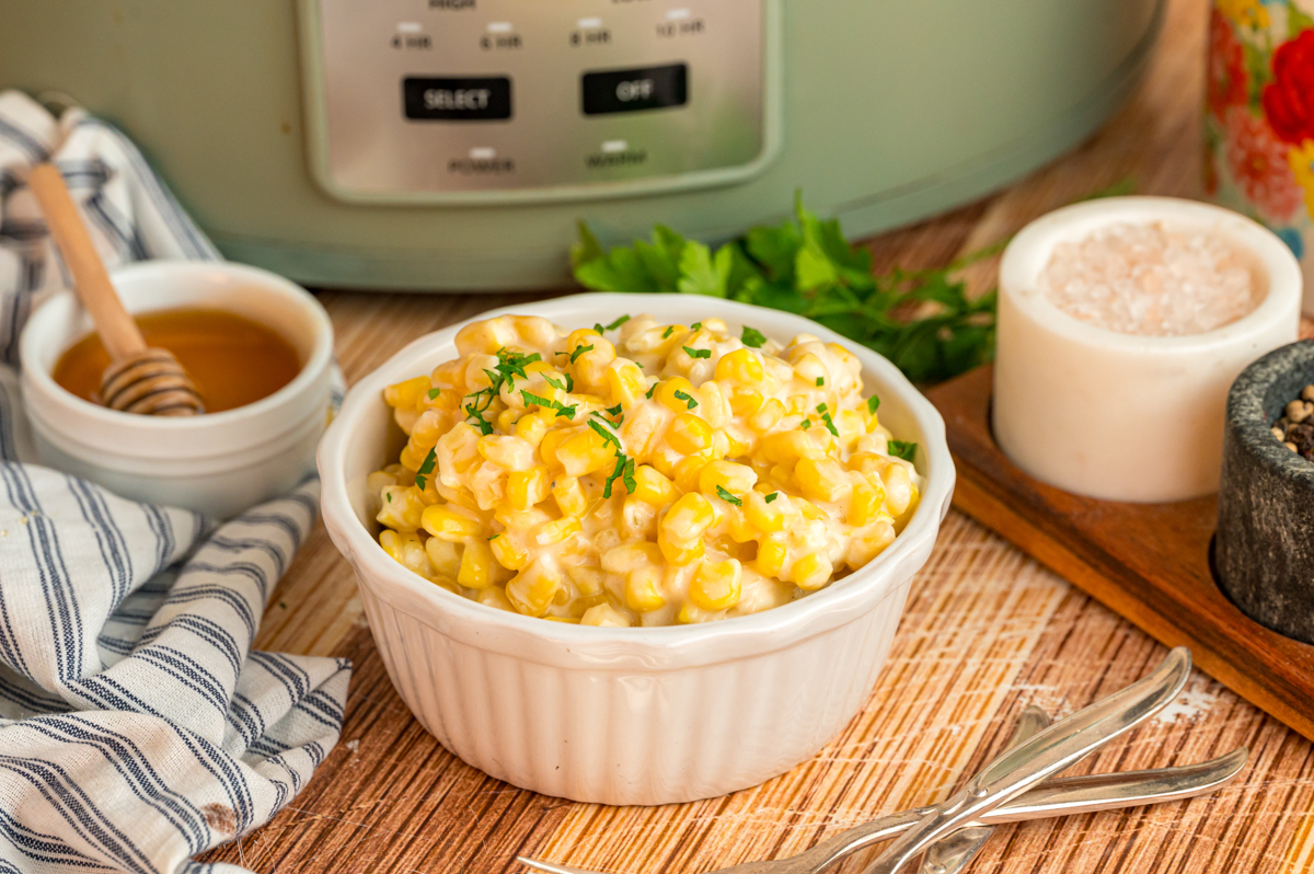 Slow cooker honey butter corn in a white bowl in front of a crockpot.