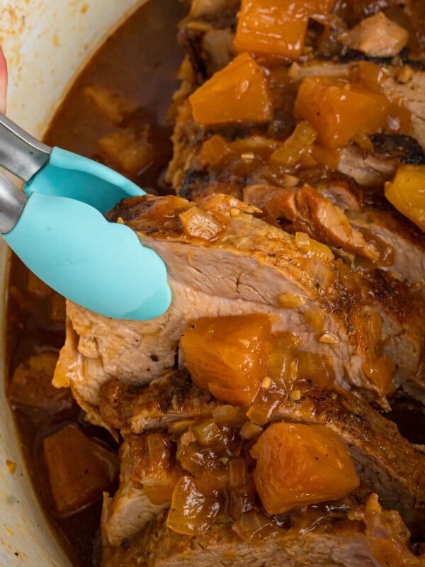 Tongs grabbing a piece of polynesian pork from a slow cooker.