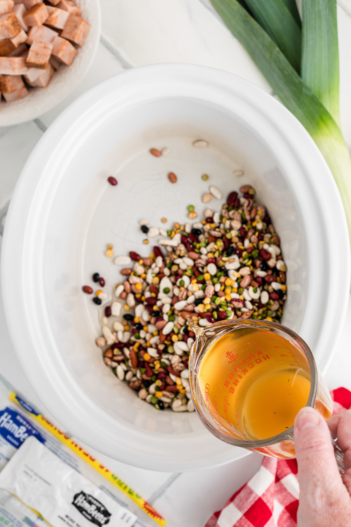 Pouring broth into a slow cooker with cajun 15 bean soup mix.