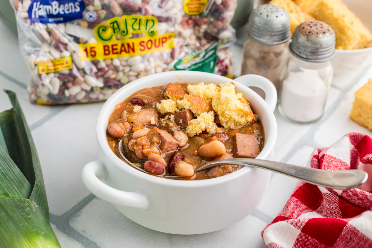 Slow cooker smoked turkey cajun 15 bean soup in a bowl with cornbread and a spoon.