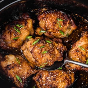 Scooping slow cooker teriyaki chicken thighs from a crockpot.