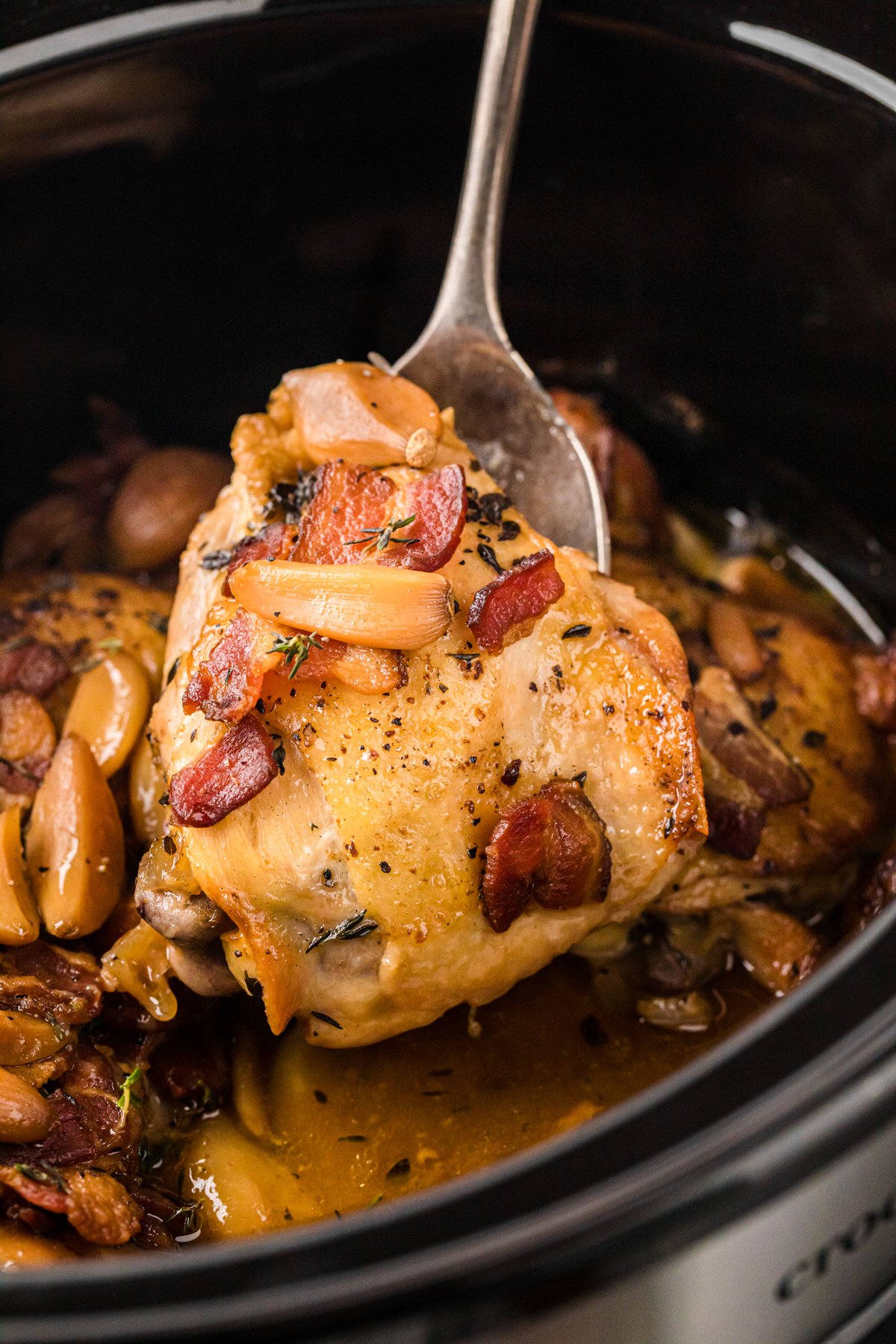 A metal spoon holding up a piece of slow cooker 40 clove chicken.