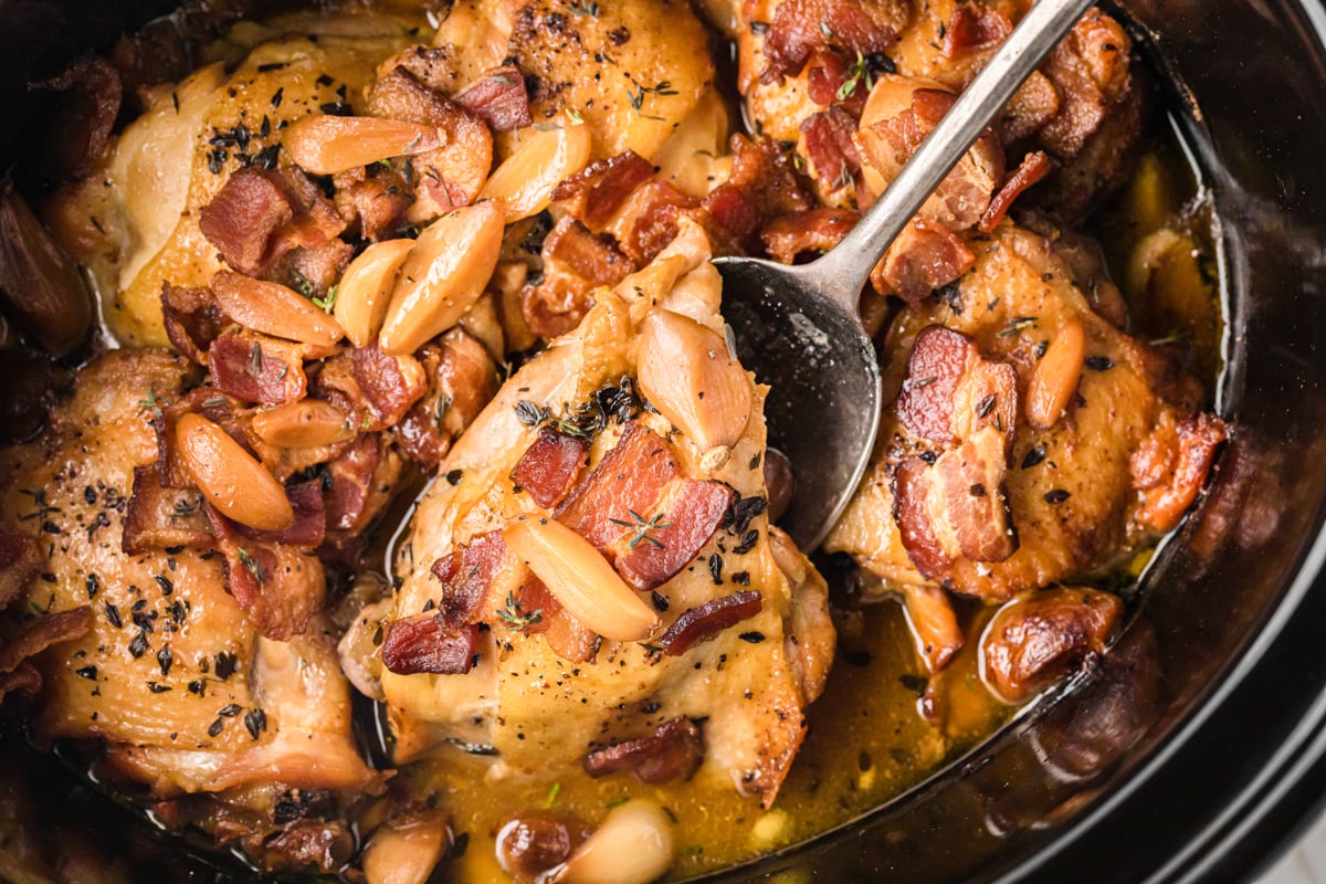 A spoon picking up a piece of slow cooker 40 clove chicken.