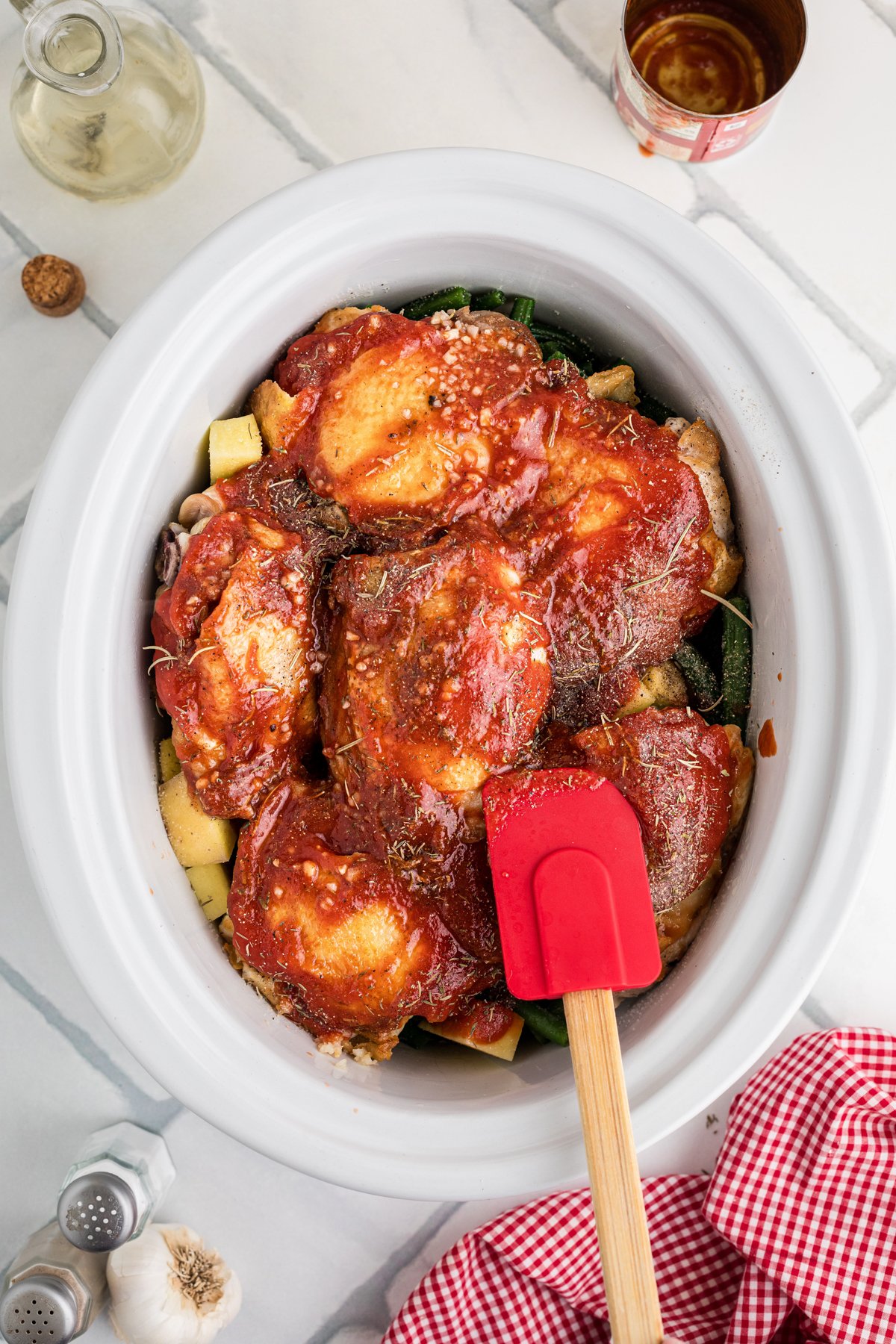 Coating chicken thighs in a crockpot with tomato sauce, garlic, and seasonings.