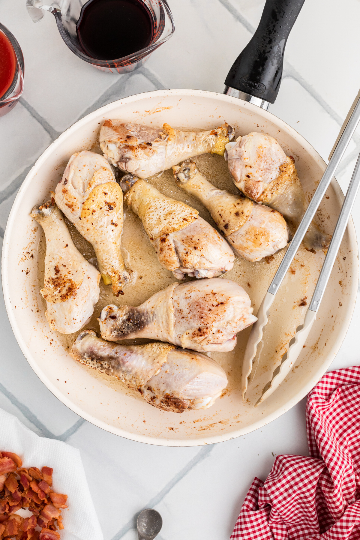 Chicken drumsticks cooking in a skillet.