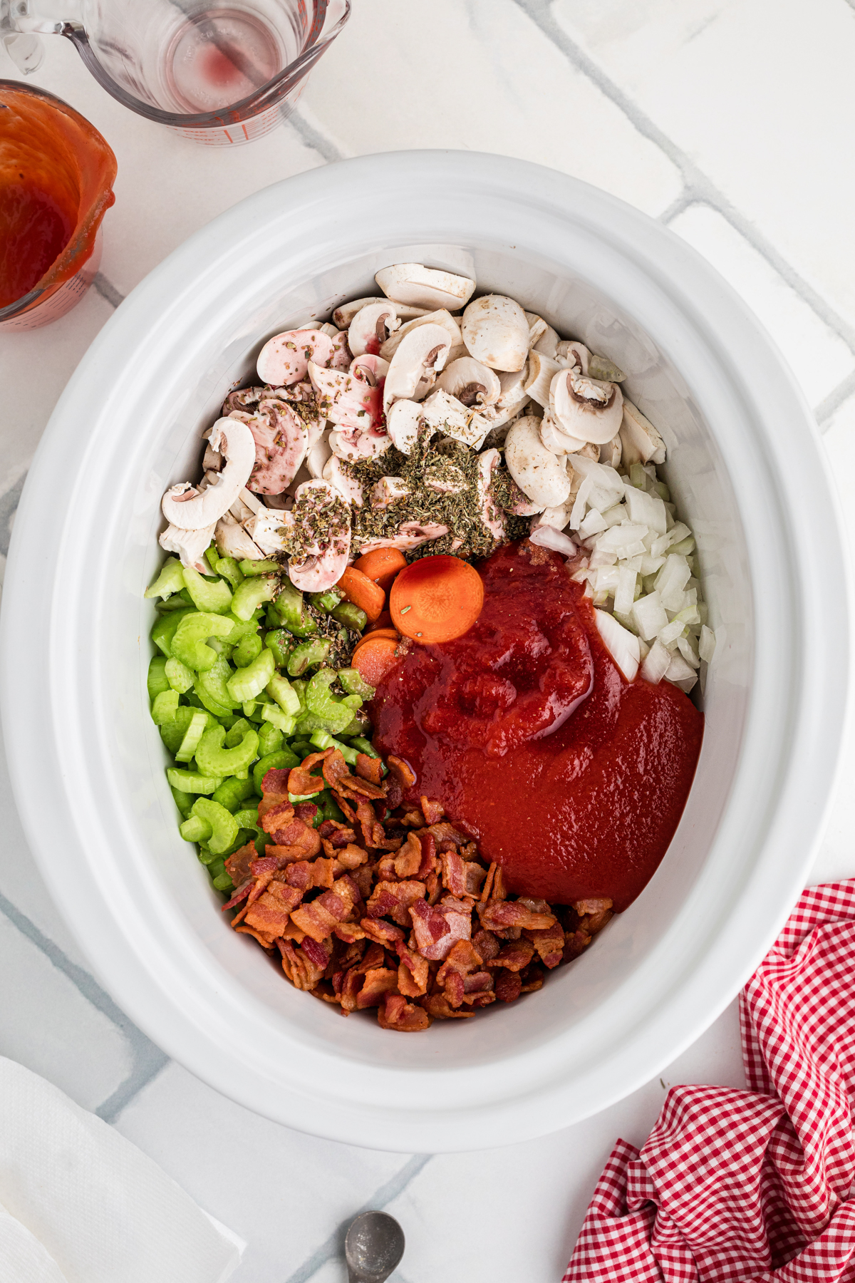 Tomato sauce and bacon added to ingredients in a slow cooker.