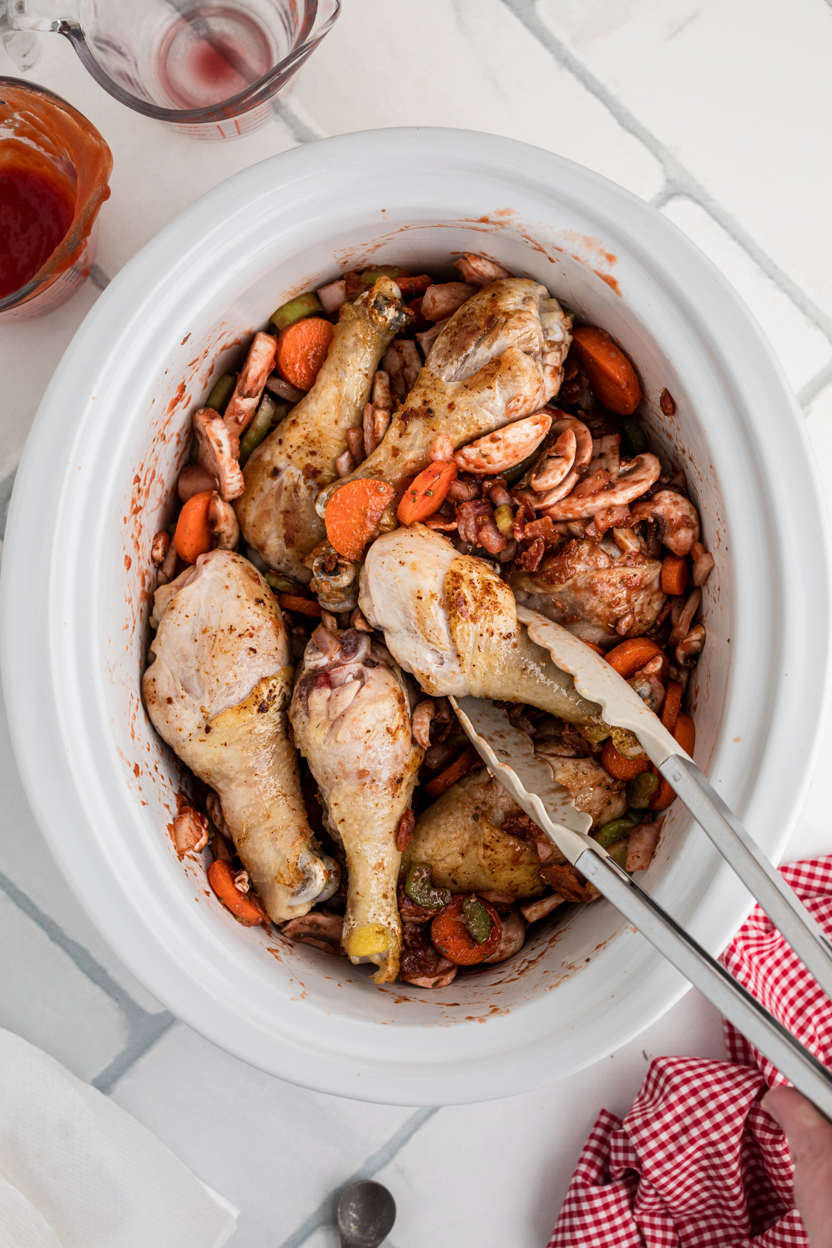 Chicken drumsticks being added to ingredients in a slow cooker.