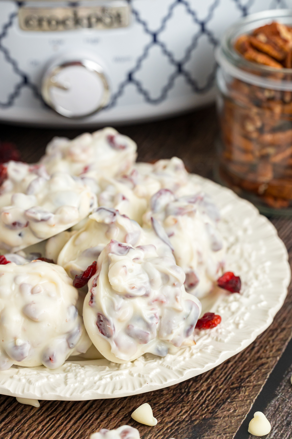 Slow cooker white chocolate cranberry clusters on a plate in front of a crockpot.