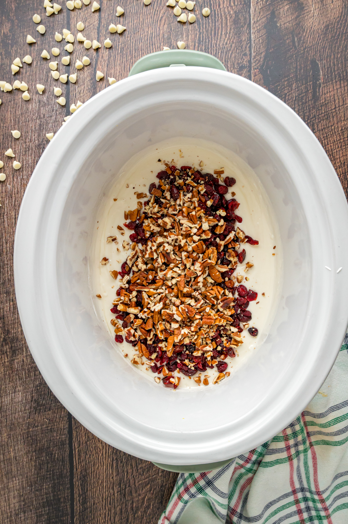 Pecans and cranberries added to melted white chocolate in a crockpot.