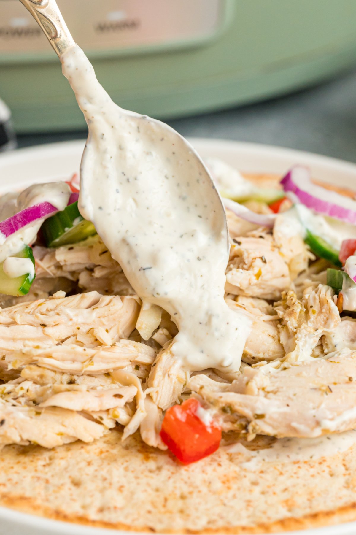 Chicken on a pita bread with sauce being spooned on.